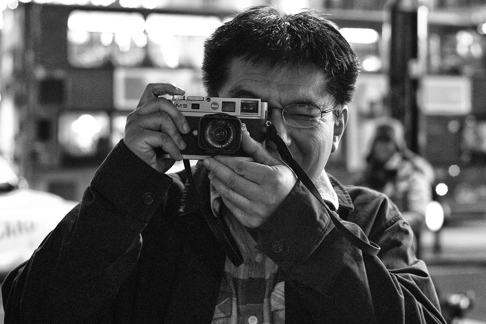  Chance encounter with another Leica street tog visiting from Seattle with his well-used M9 and 28mm Elmarit. Unfortunately his battery was flat so no reciprocal photo. Taken at Piccadilly Circus with 35mm 'Lux, f/2.8 at 1/125s, 800 ISO,  50% crop. 