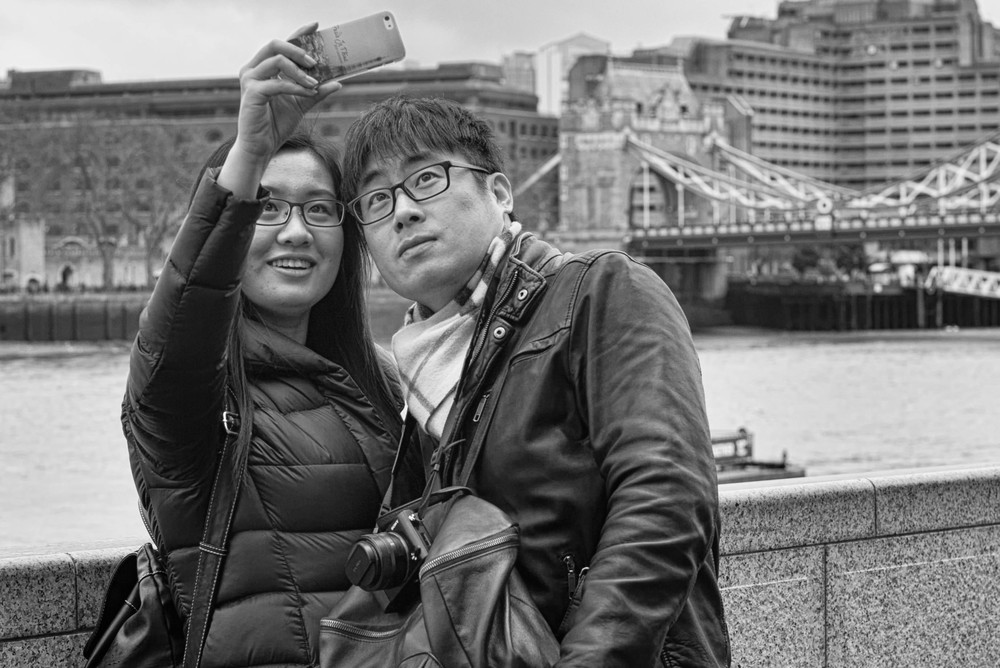 Never miss a selvesie in front of Tower Bridge: In this case the far more competent Sony RX1 was left neck dangling while the versatile iPhone was pressed into service. Judging from the phone cover, these two trophy hunters have just arrived from the Eiffel Tower and want to add to their collection. Photo Mike Evans.
