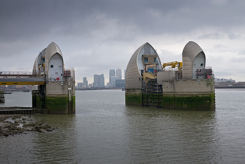 The skyscrapers of Canary Wharf glimpsed through the sleeping maw of the mighty barrier. Photo George James.