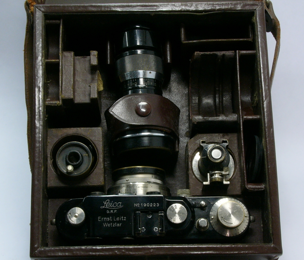 This kit includes the camera and 50mm lens, a further 105mm lens, a universal viewfinder, film cassette and filters. To the top left is an angular viewfinder would have sat and the lens slot to the right was intended for a 35mm lens--not present in this kit. It is an extremely compact way of carrying a full complement of photographic equipment. Note the near identical layout to the contemporary advertisement above.