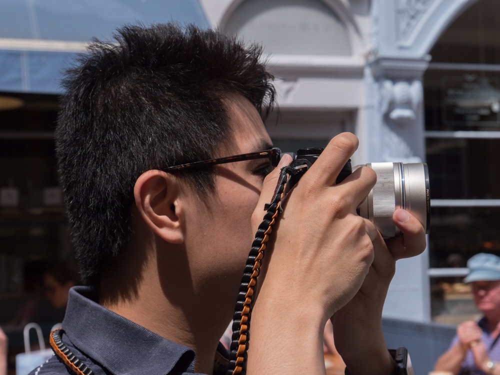 Back to street photography and a fellow photographer at work — with what appears to be another Panasonic GX8 and the beautiful Olympus M.Zuiko Digital ED 75mm f/1.8