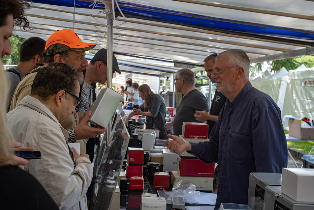 Ivor, in the orange camouflage hat, discusses a boxed Leica film camera with Belgium