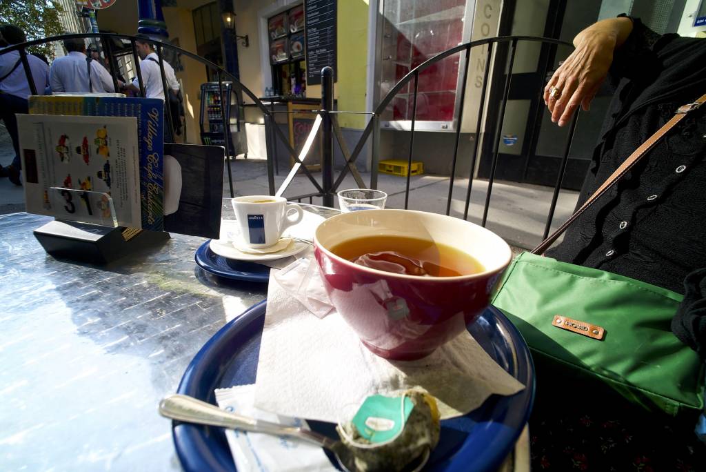 What I get from, or like about, this picture is the sense of relaxation from the hand draped over the bit of metal fence, and the repeating patterns of curves; the fencing, the cups, the saucers, table, glass, spoon, buttons, and then the three fellas otherwise occupied at the upper left of the picture. The lower part of the picture is mainly curves, but the upper part is mainly the radiating straight lines of the shopfronts ..and the spokes of the fencing join the two.