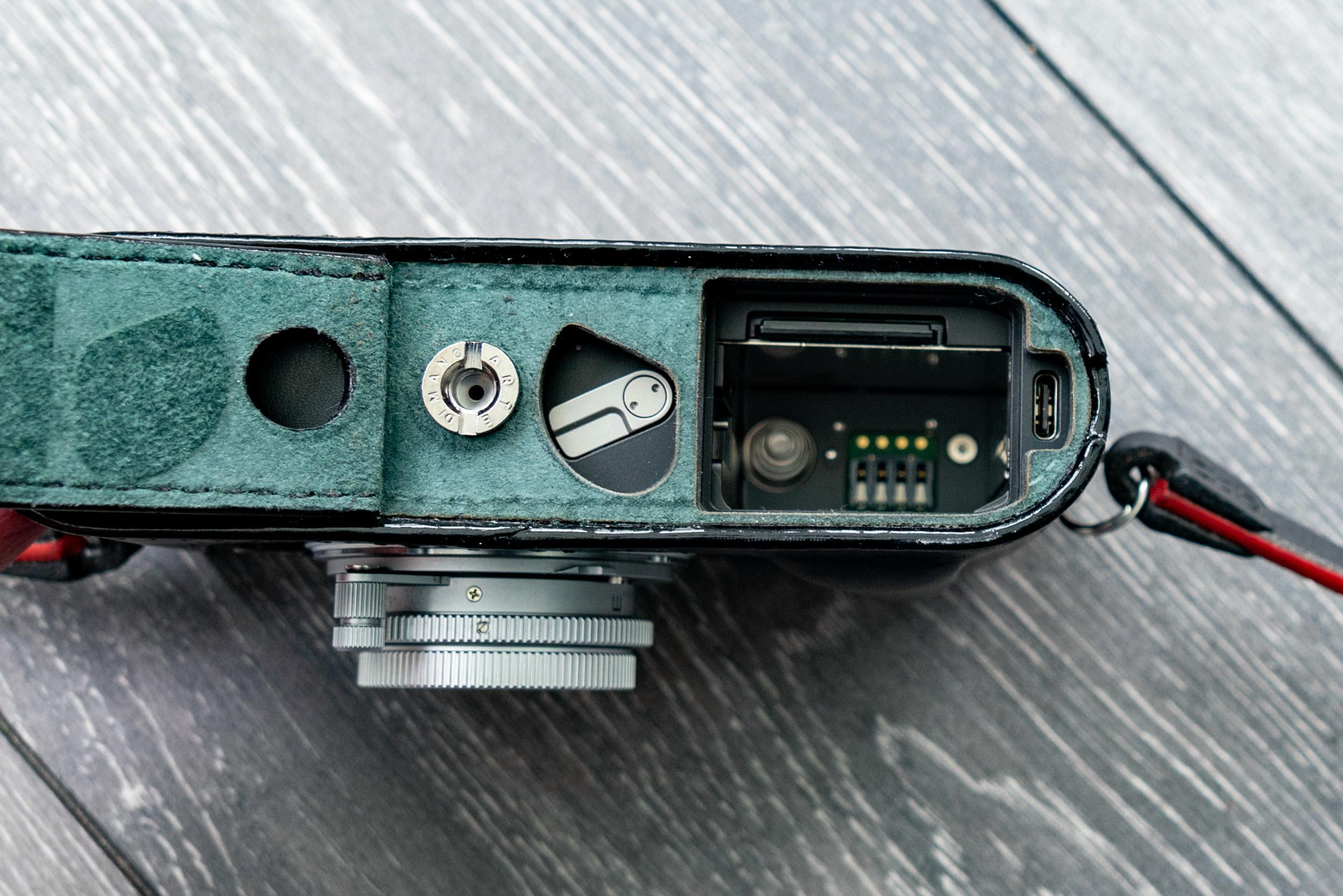 Battery compartment of the M11. The SD card slot is protected by an overhang on the battery bottom and this means that the battery must be removed in order to access the card. In this shot, the M11 is in the Arte di Mano half-case, showing the opening flap and the secure tripod-mount fixing. The USB-C port, to the far right, is almost an afterthought and it's perhaps the only place they could find to avoid messing with the camera's internals.