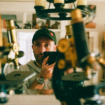 Picture of man holding a camera standing beside microscopes