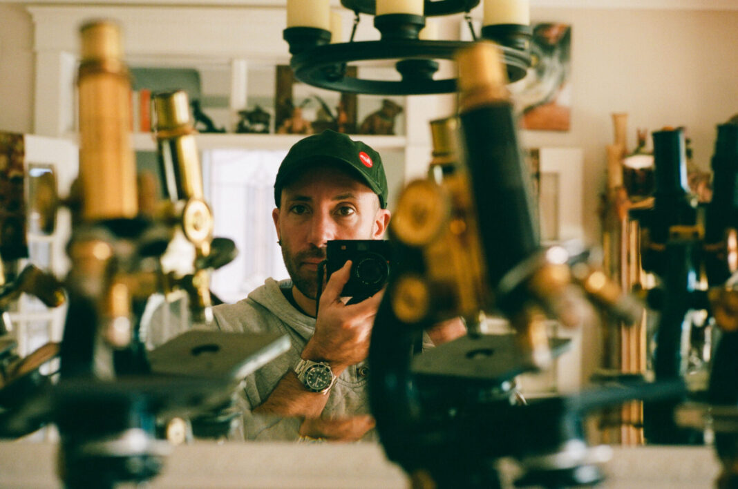 Picture of man holding a camera standing beside microscopes