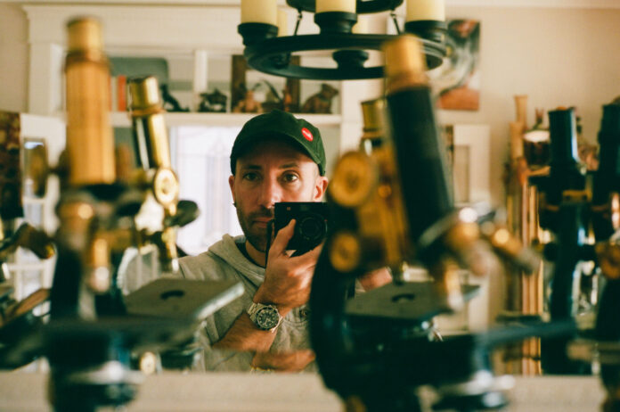Picture of man holding a camera standing beside microscopes