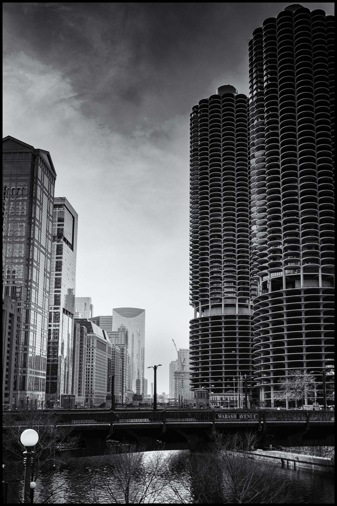 Black and white image of a cityscape featuring modern skyscrapers and a river, with a bridge labelled 'Wabash Avenue' and trees along the riverbank.