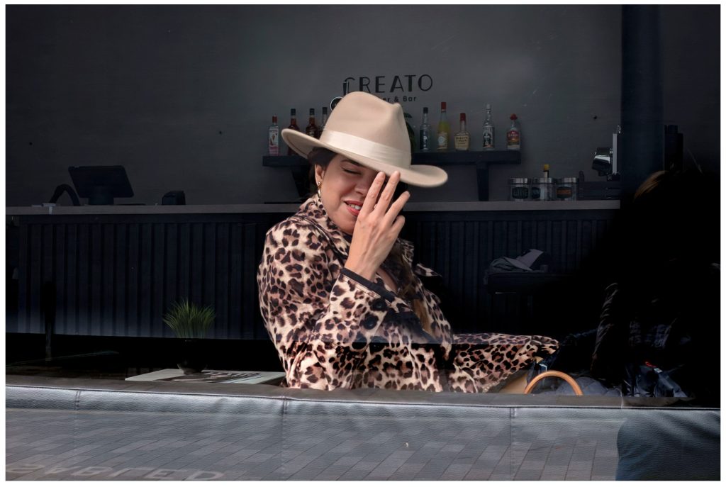 Woman touching brim of hat, shot through a window