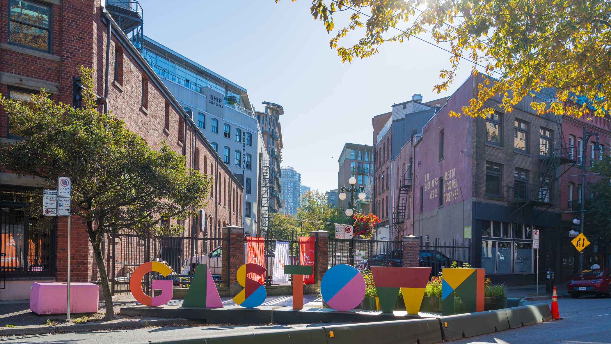 Colorful 'GASTOWN' sign in the historic Gastown neighborhood of Vancouver, surrounded by brick buildings and greenery.