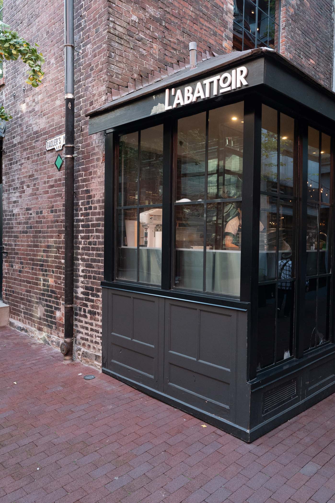 Exterior view of L'Abattoir restaurant, featuring a brick wall and large glass windows, located in a charming alley.