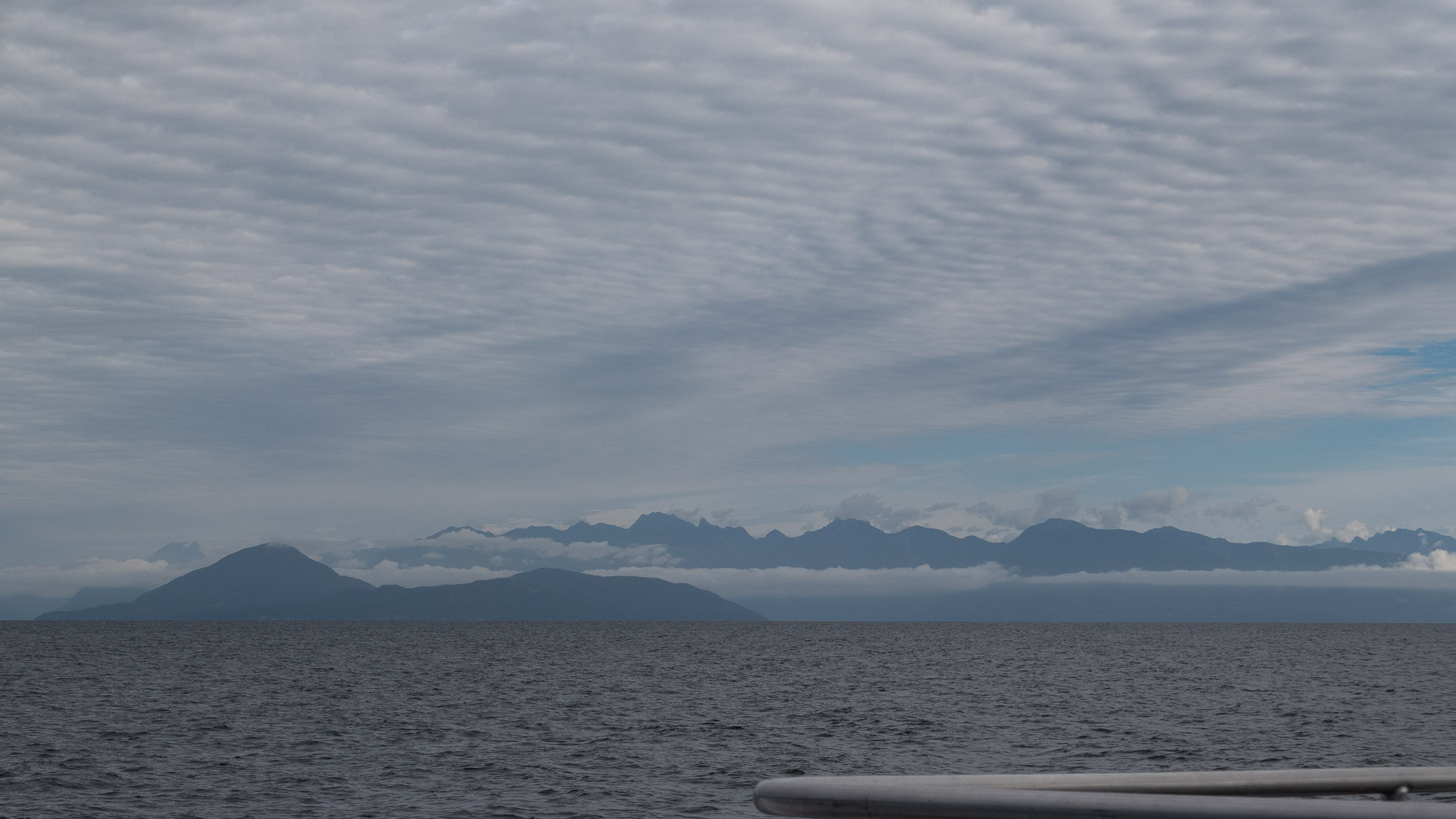 A view of distant mountains across a calm sea under a cloudy sky, taken from a ferry.