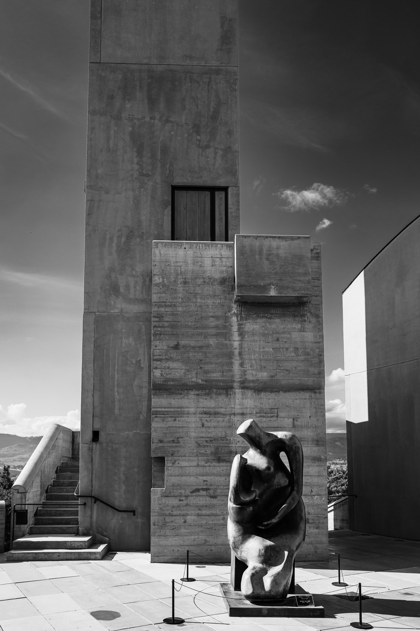 Black and white image of a concrete structure with a tall tower and a sculpture at its base.