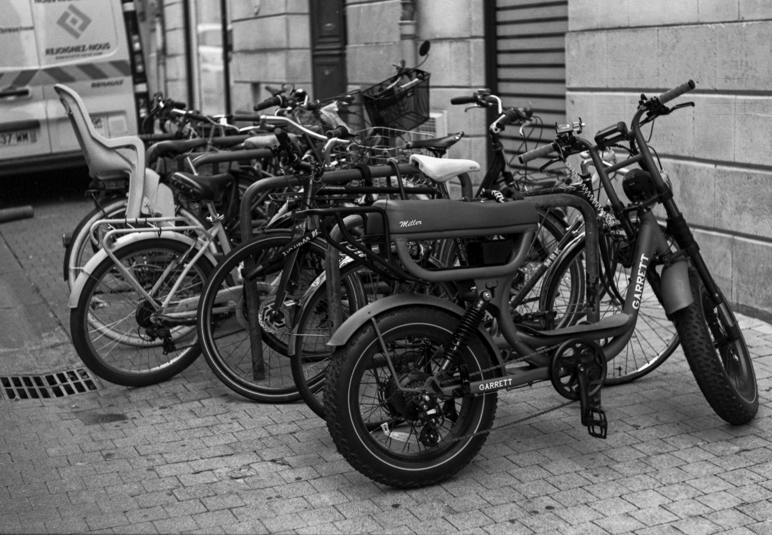A row of parked bicycles on a cobblestone street, including a distinctive electric bicycle with the label 'GARRETT'.