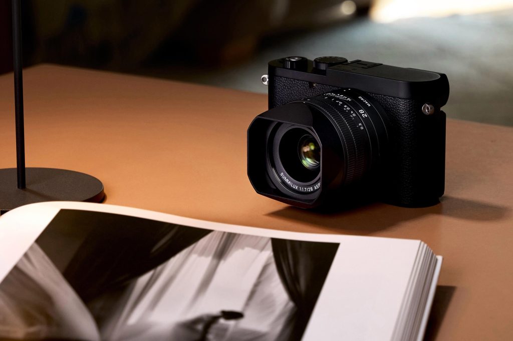 Leica Q3 Monochrom camera on a table next to a photography book, featuring a matte-black finish and leatherette cover.