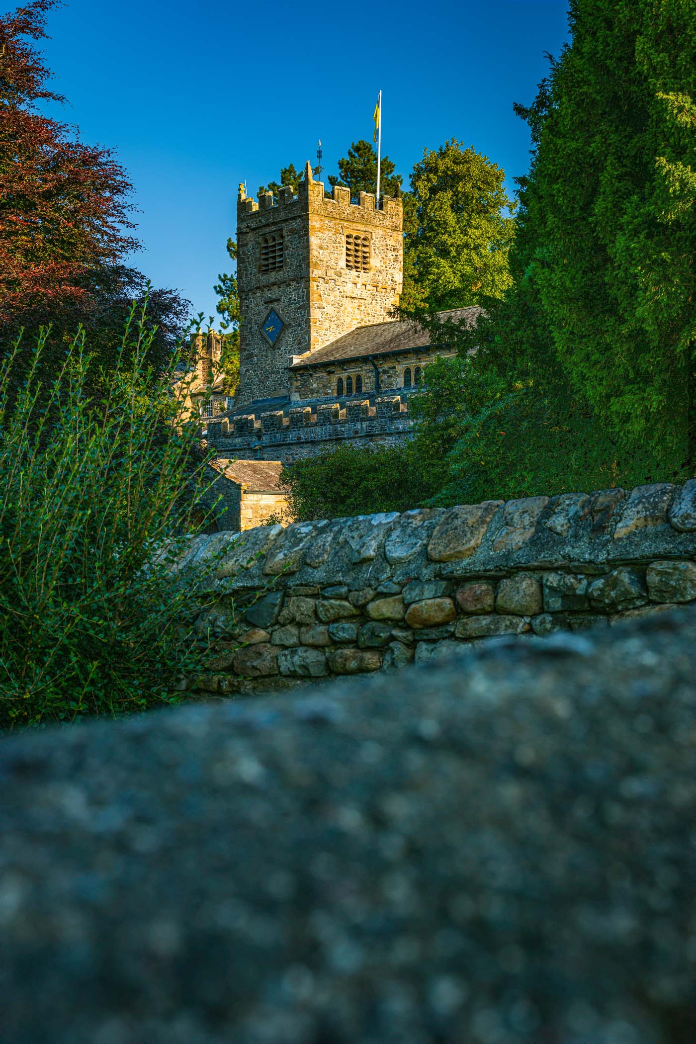 A stone church tower rises amid greenery, framed by a blue sky.