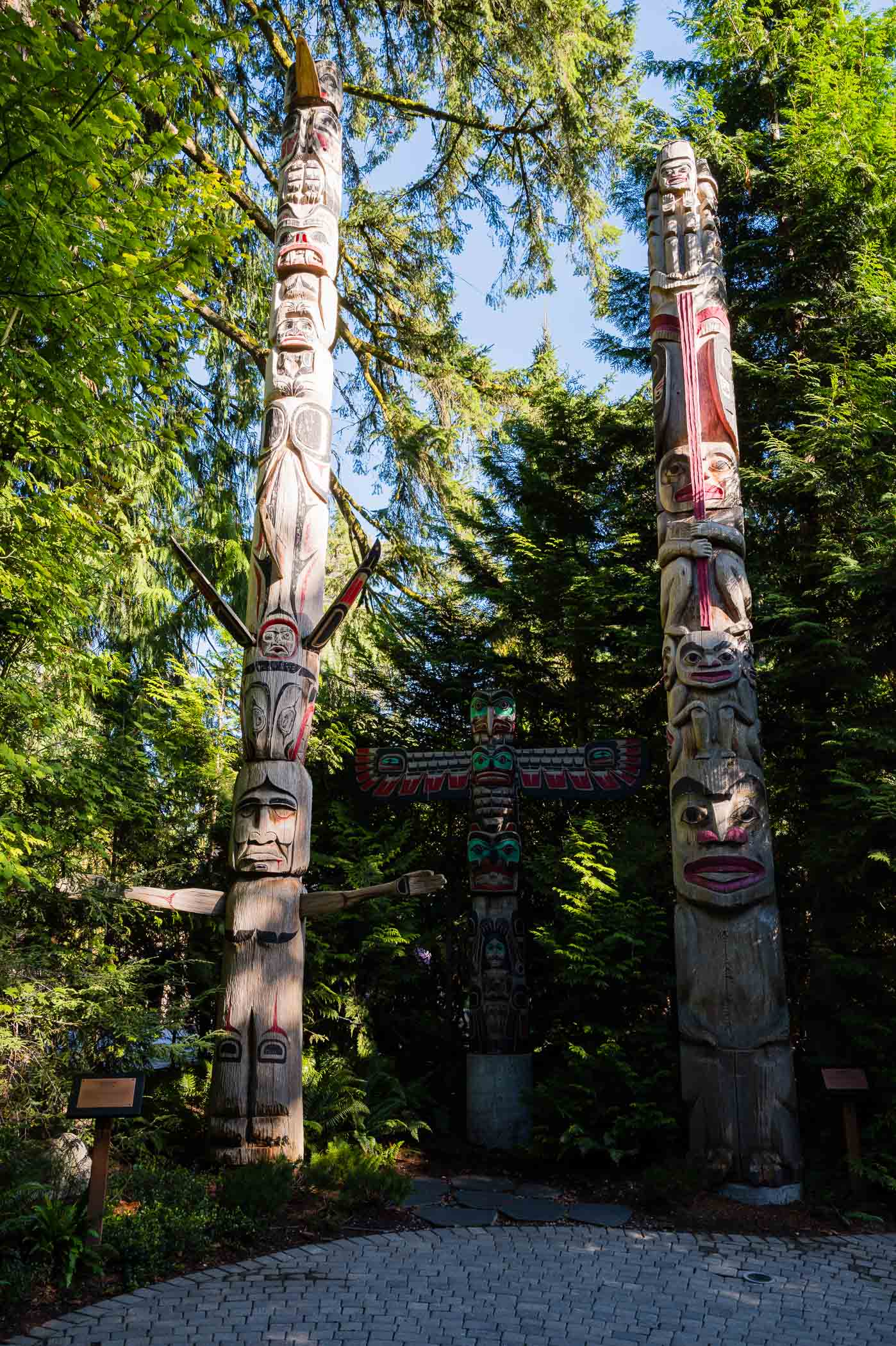 Two large totem poles surrounded by green trees, representing Indigenous art and culture.