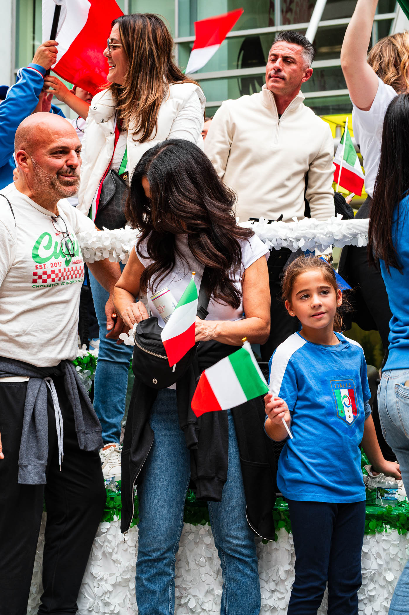 A group of people celebrating Columbus Day in Chicago, holding small Italian flags. The scene captures the festive atmosphere with individuals dressed casually and enjoying the parade.