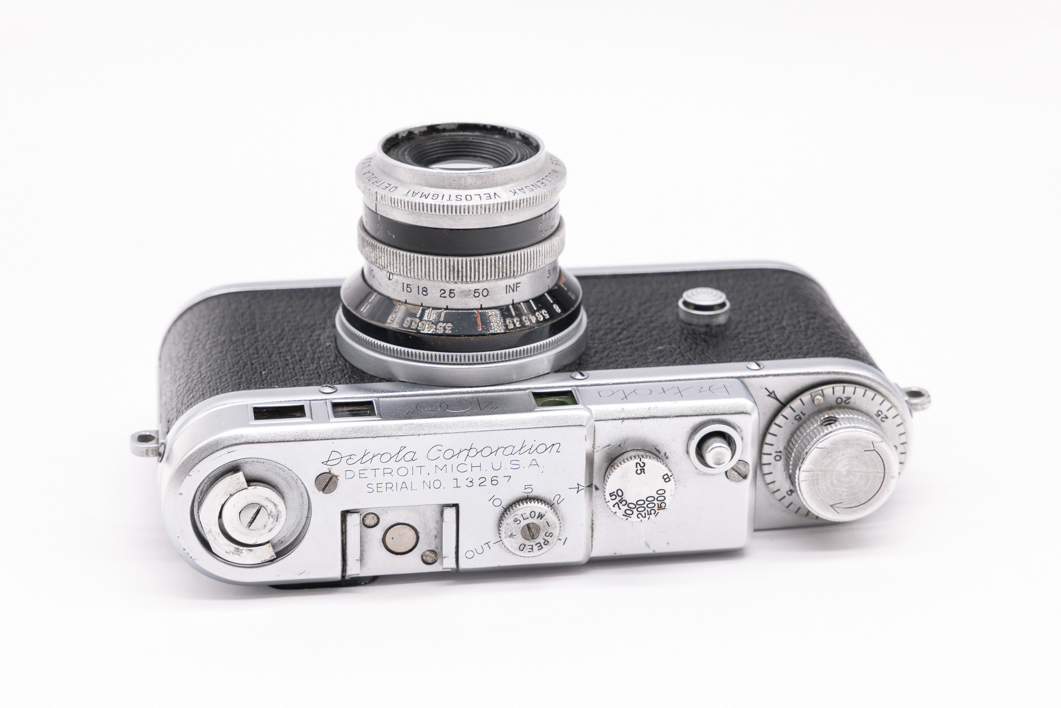 Detailed view of a Detrola 400 camera, featuring a metallic body, 50mm Velostigmat lens, and engraved markings indicating its manufacturer and serial number.