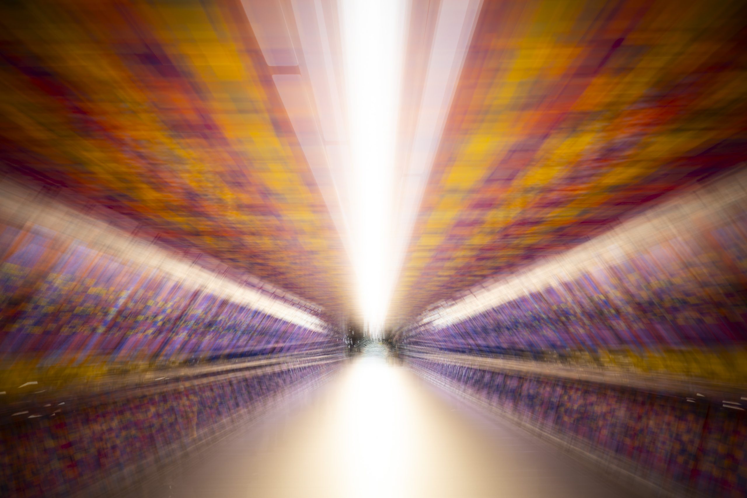 An abstract image featuring blurred lines and vibrant colors, suggesting motion and energy. The composition directs attention towards a bright light source at the center, creating a dynamic visual effect.