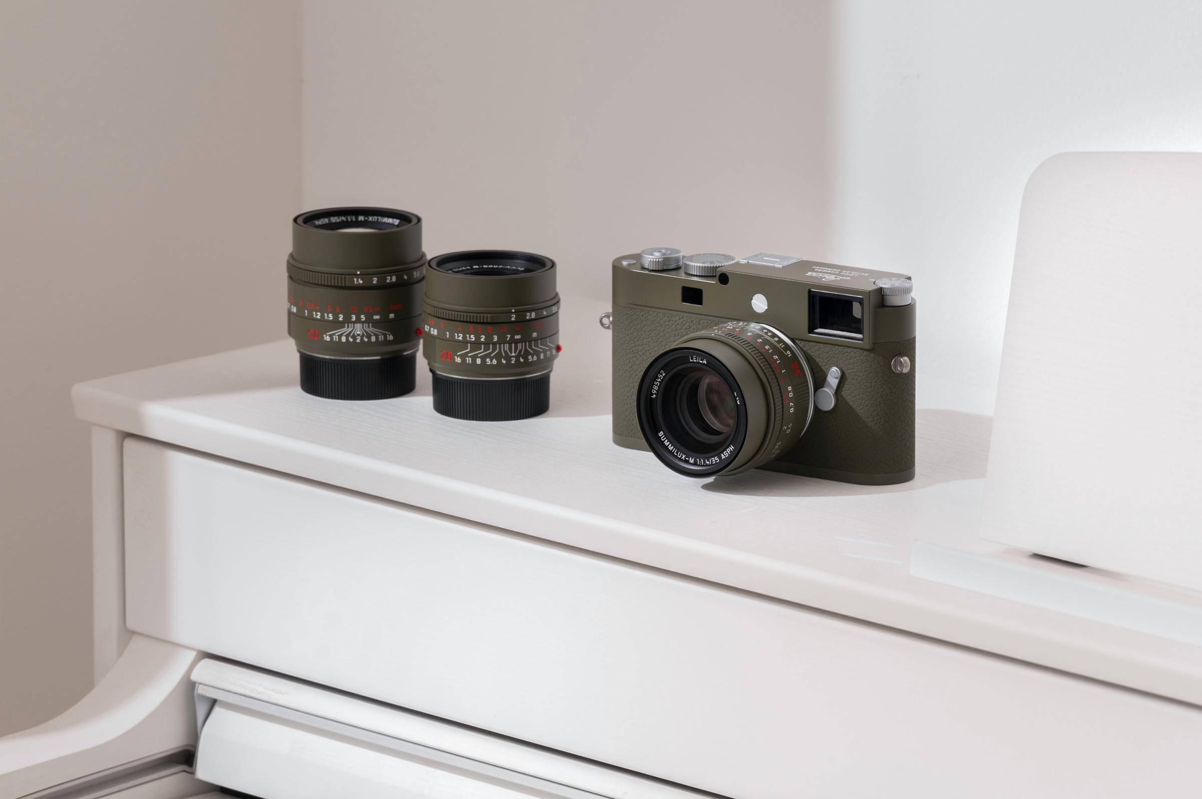 A Leica camera in matte olive green with two complementary Safari edition lenses placed on a white surface.