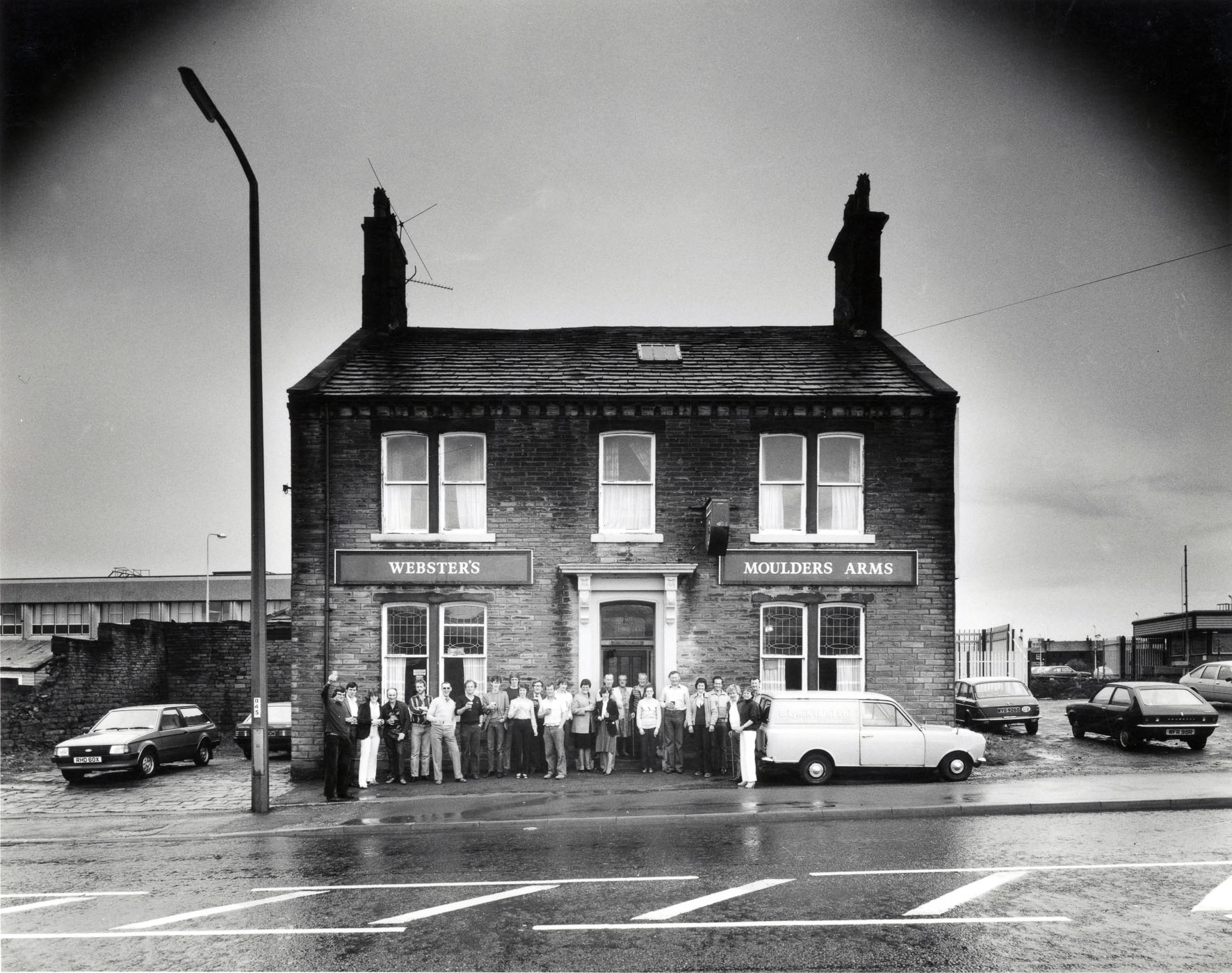 Historic black and white photograph of the Moulders Arms pub with a large group of people gathered outside, showcasing the community hub aspect of local pubs.