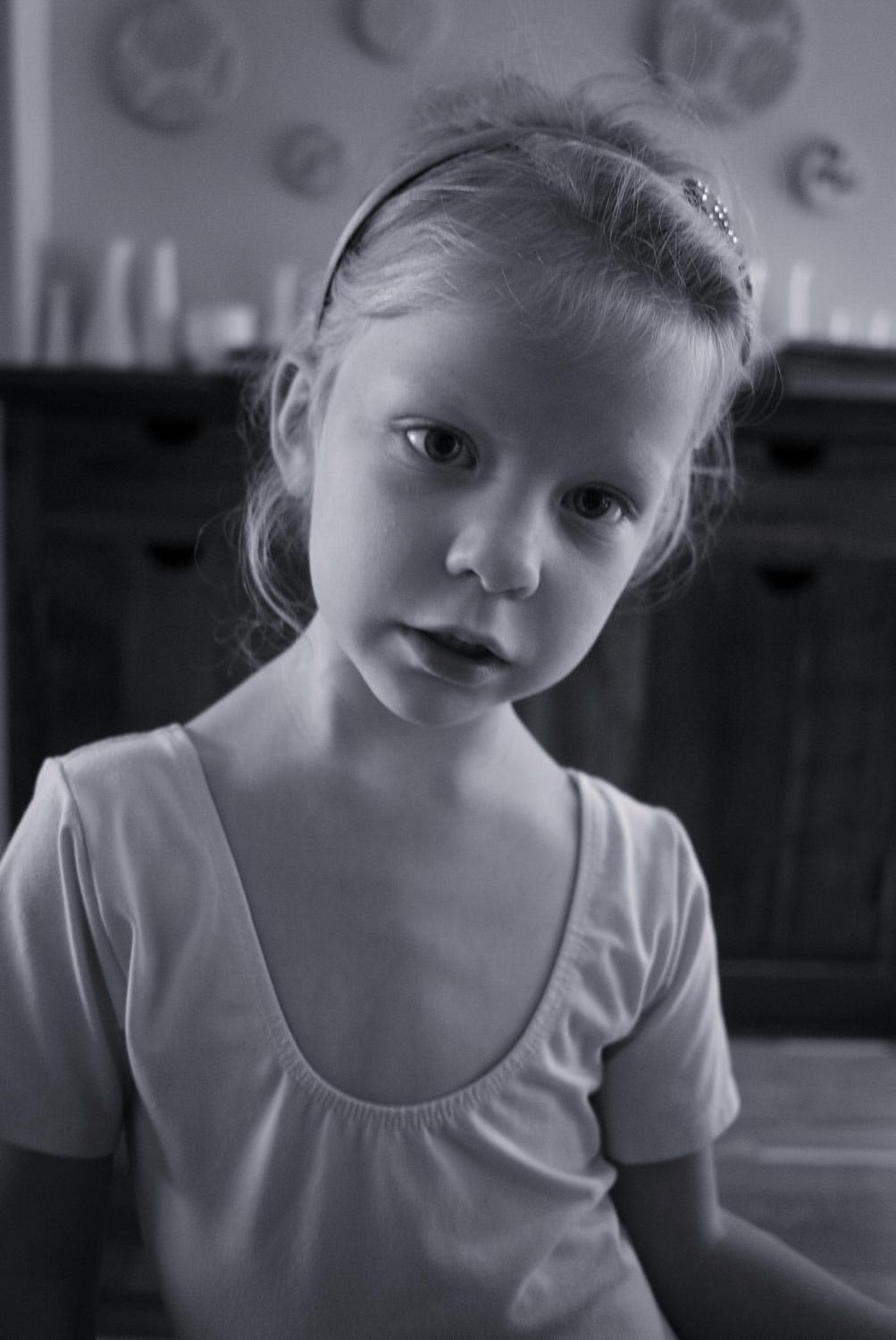 A young girl in a light-coloured top, looking thoughtfully at the camera in a black and white setting.
