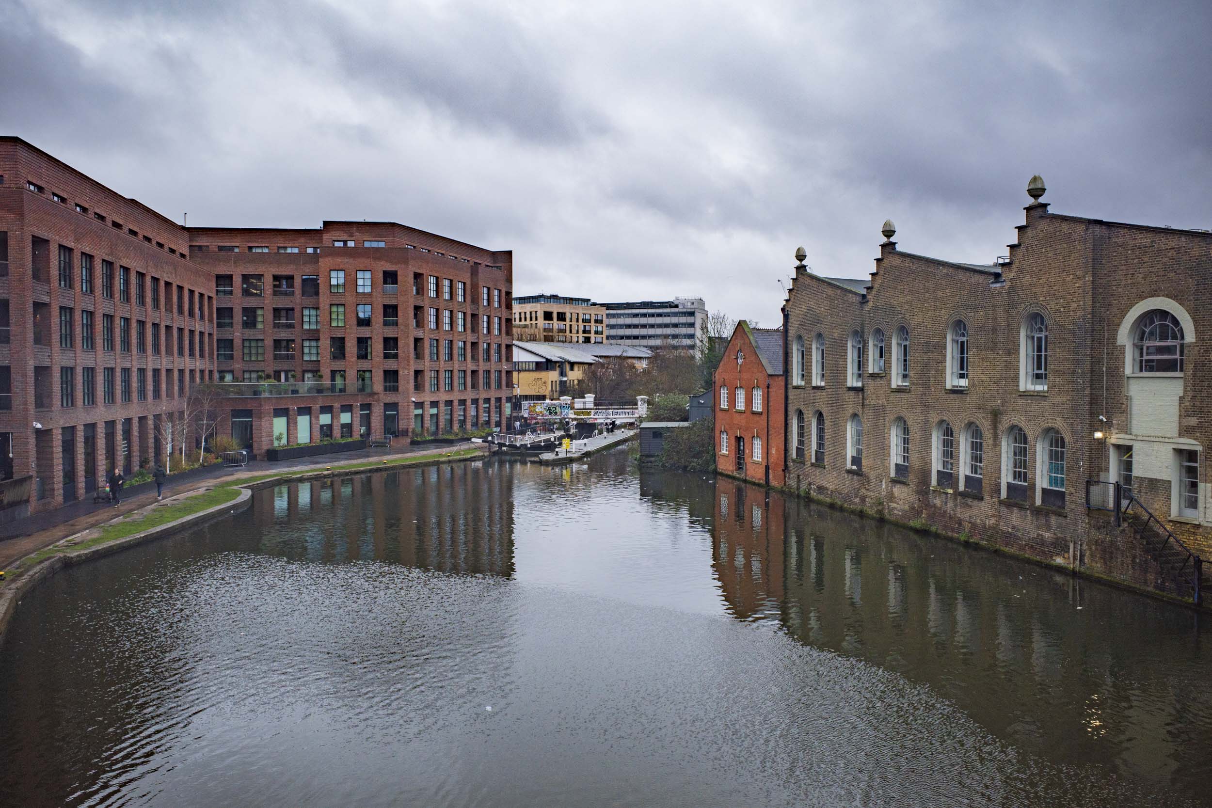 A view of a canal surrounded by modern and historical brick buildings under a cloudy sky.