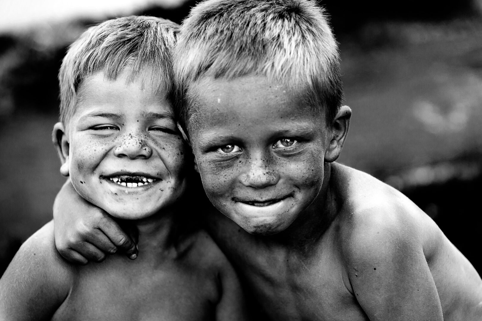 Two smiling boys with freckles, embracing each other, captured in a black and white photo.