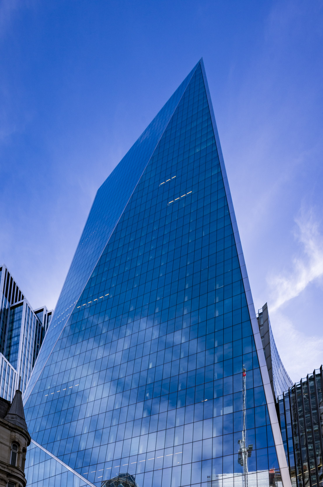A view of a modern glass skyscraper with a triangular shape, reflecting the blue sky and clouds.