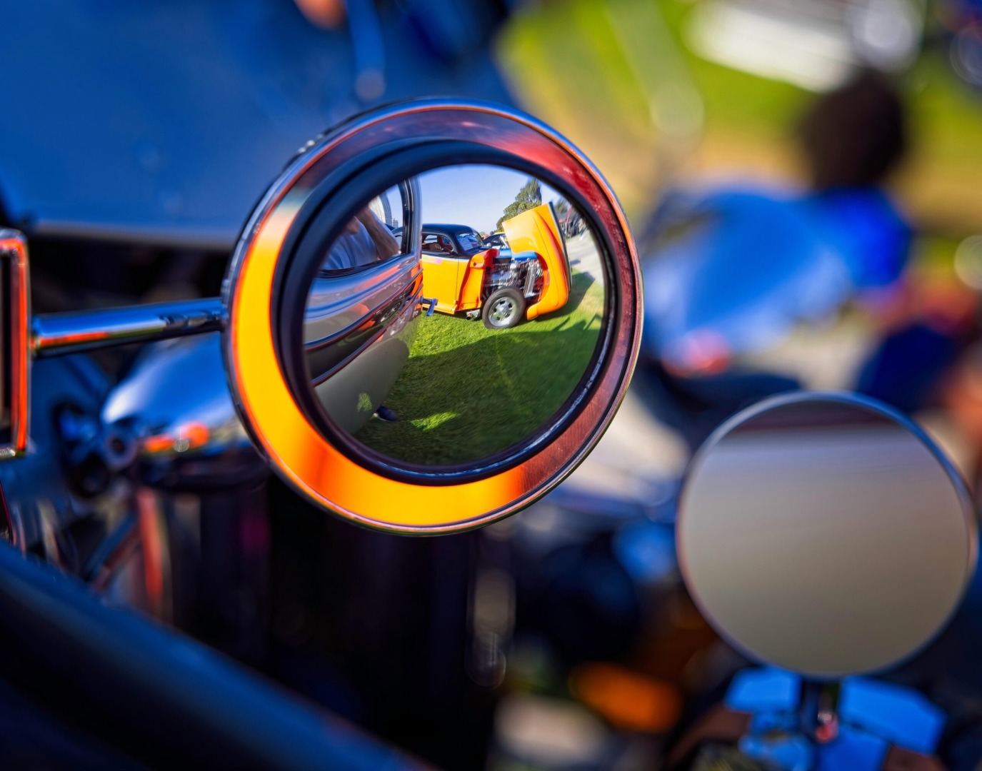 Close-up of a vehicle's side mirror reflecting a classic car and grassy background.