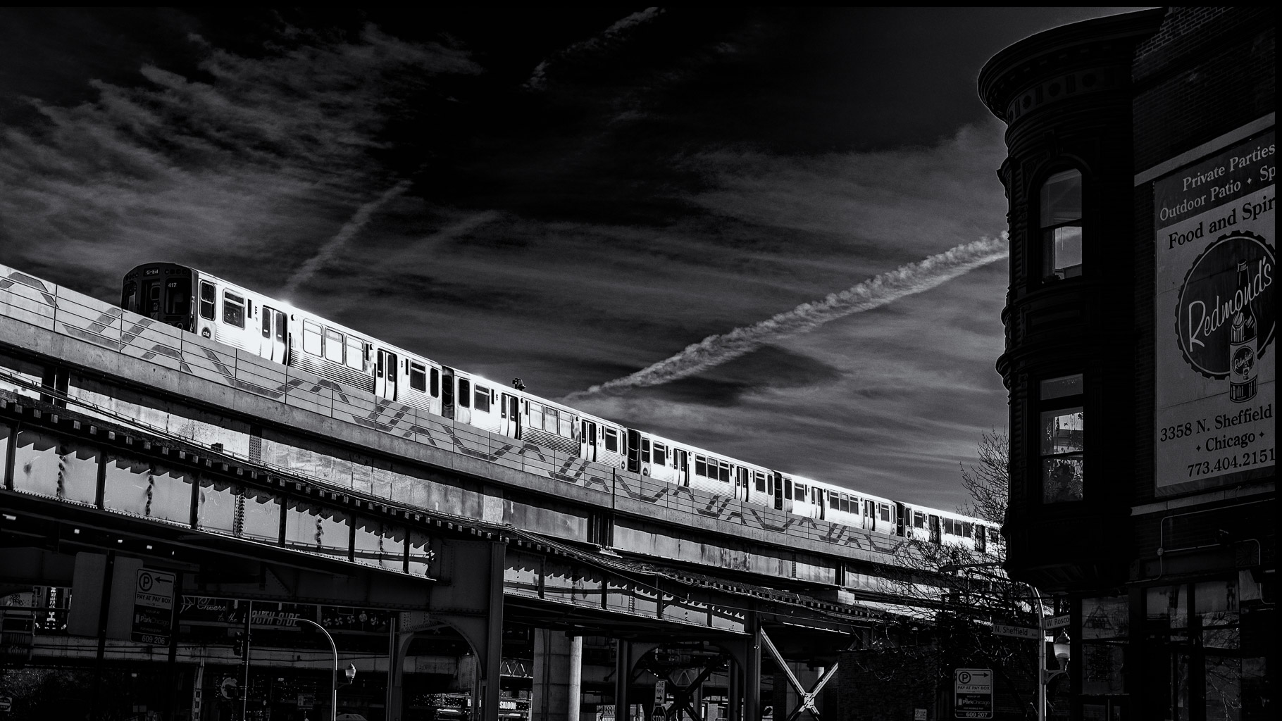 Black and white image of a train on elevated tracks with a building on the right, featuring a sign for Redmond's in Chicago.