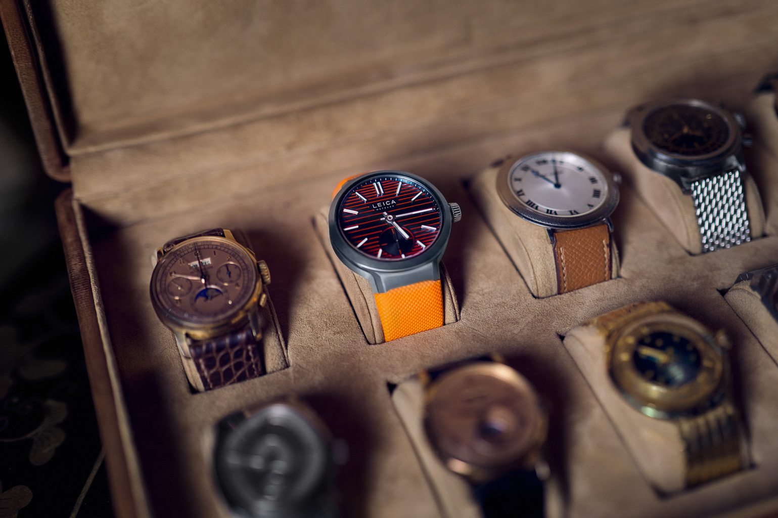 A selection of luxury watches displayed in a watch case, featuring a prominent watch with a red and orange design in the center.