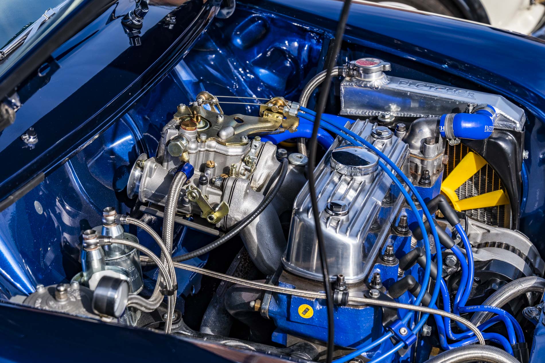 Close-up view of a car engine showing metallic components, including a polished valve cover, fuel lines, and blue hoses.
