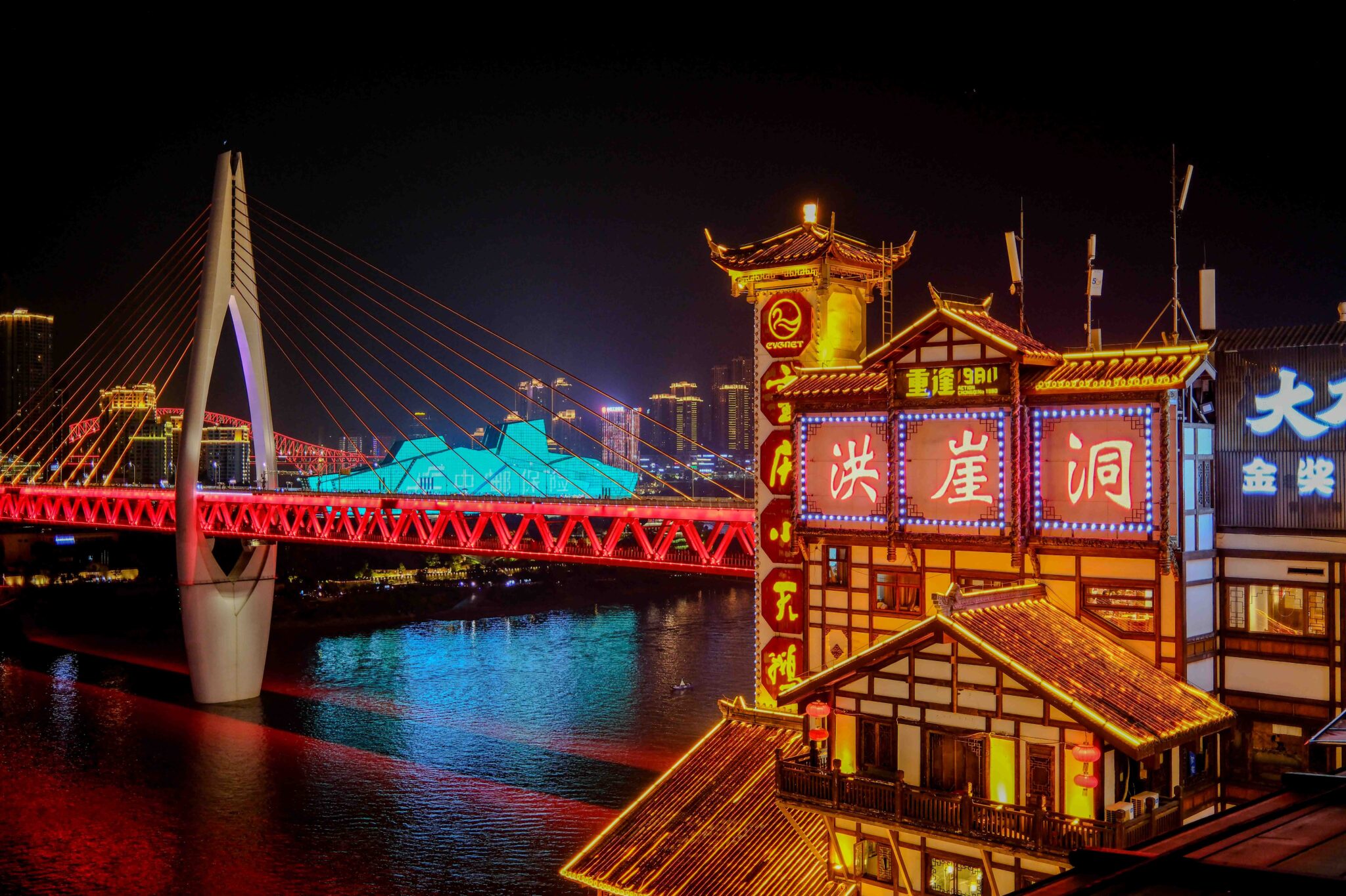 Illuminated buildings and a bridge over a river at night in a city.