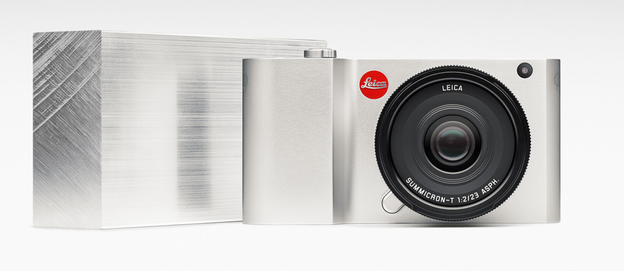 A sleek silver Leica camera with a large lens, positioned next to a metallic block.