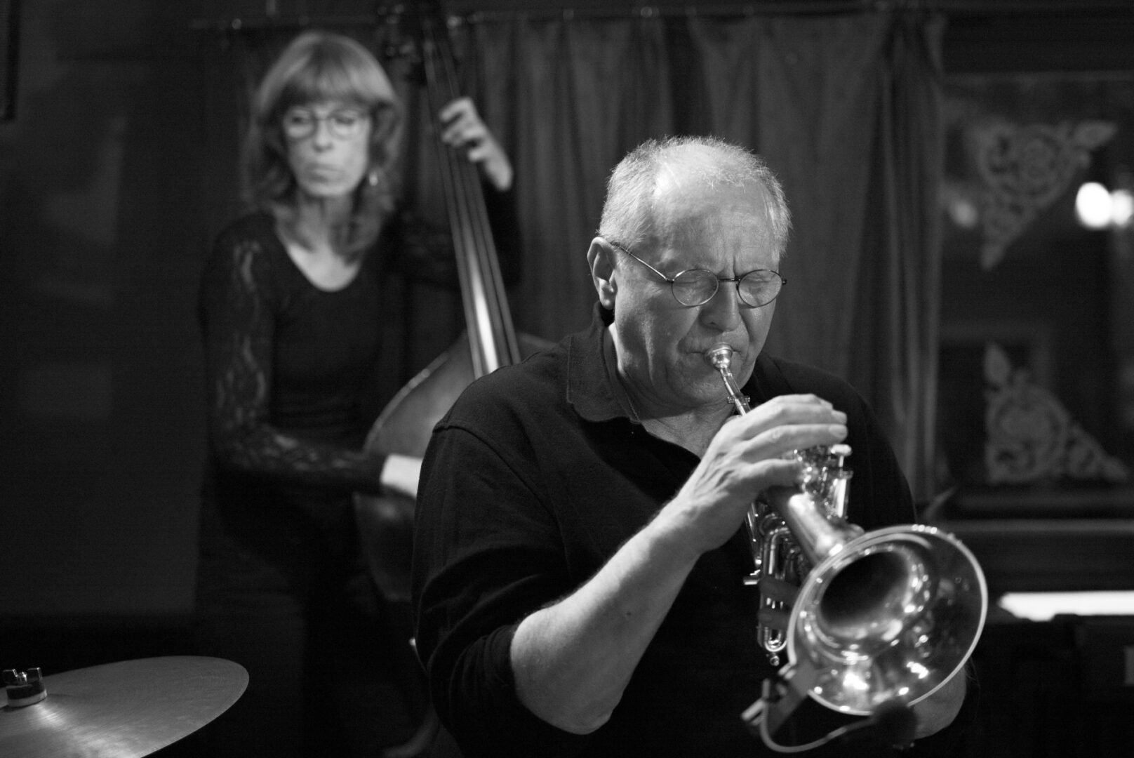 M246 A musician playing the trumpet in a jazz club, with a bassist visible in the background.