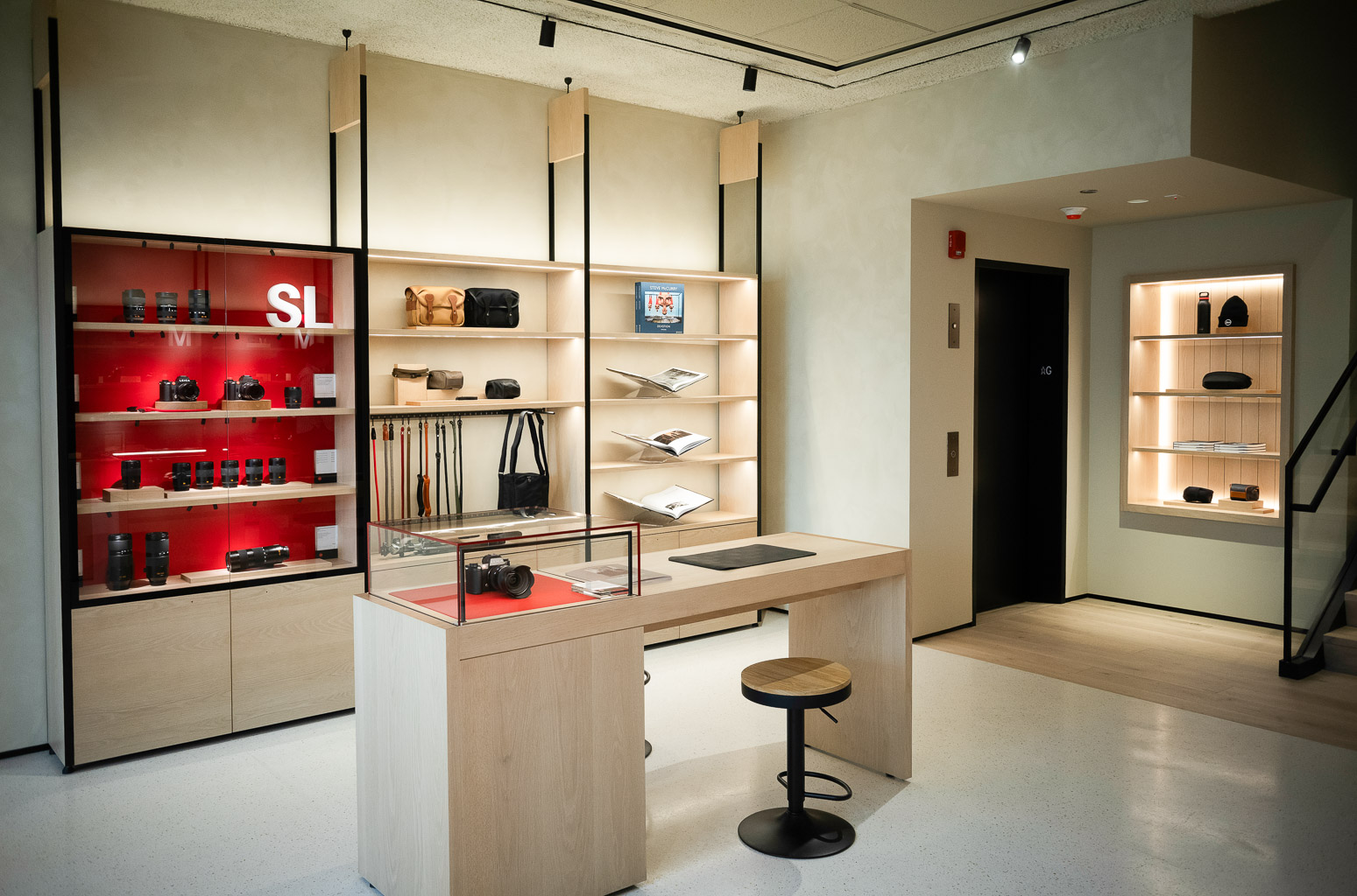 An interior view of a modern retail store showcasing shelves with photography equipment and accessories, a display counter, and a wooden stool.