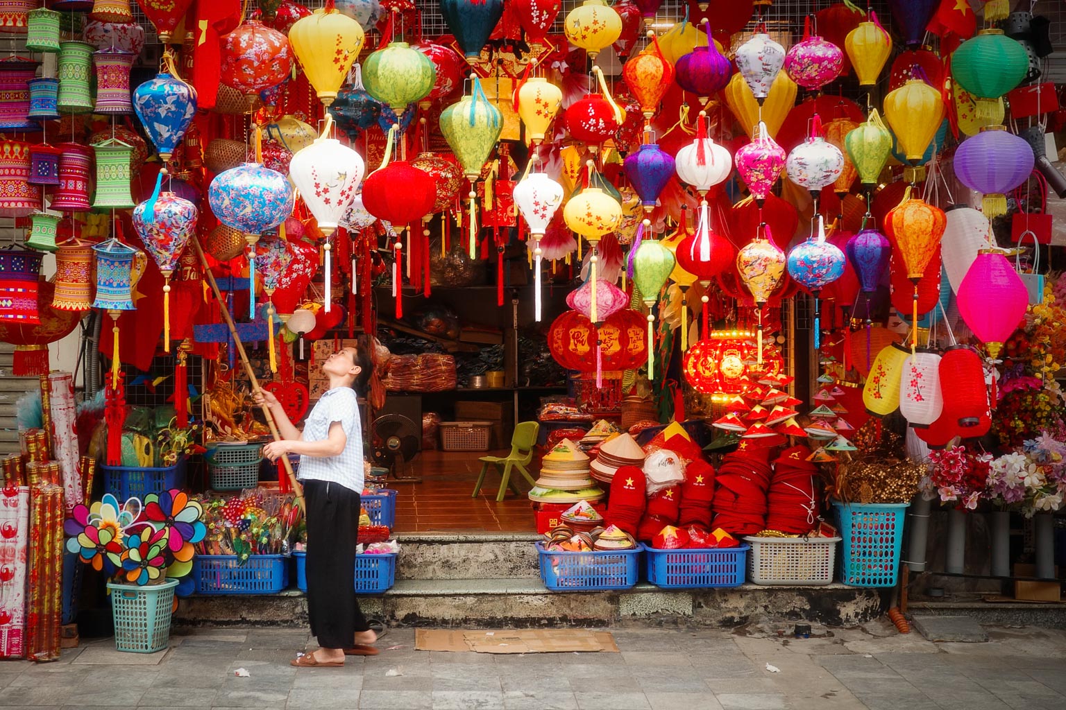 A child playing with colorful lanterns at a vibrant street market, surrounded by an array of decorative items and floral displays.