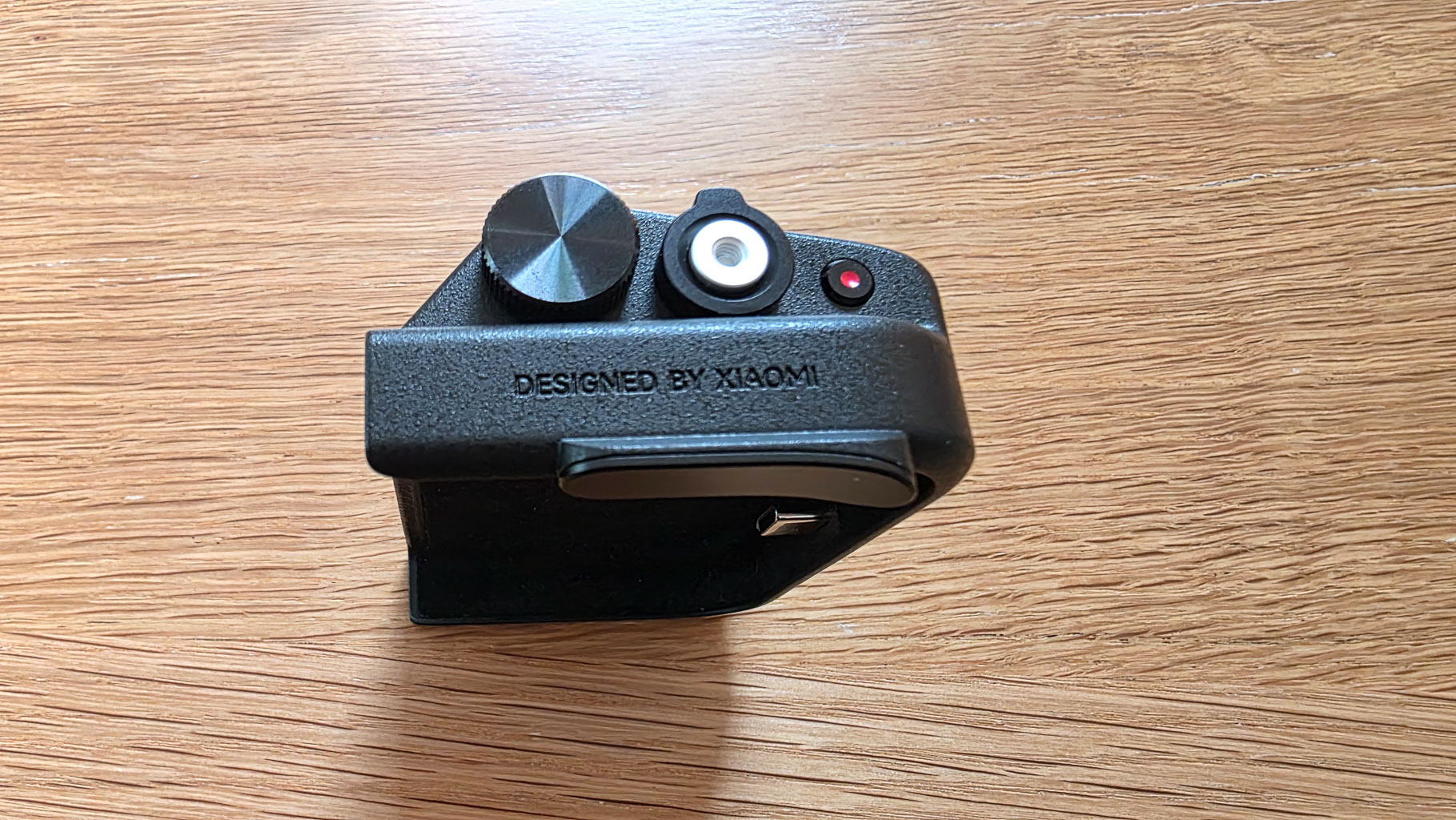 A black device with buttons and a dial, labeled 'DESIGNED BY XIAOMI', placed on a wooden surface.