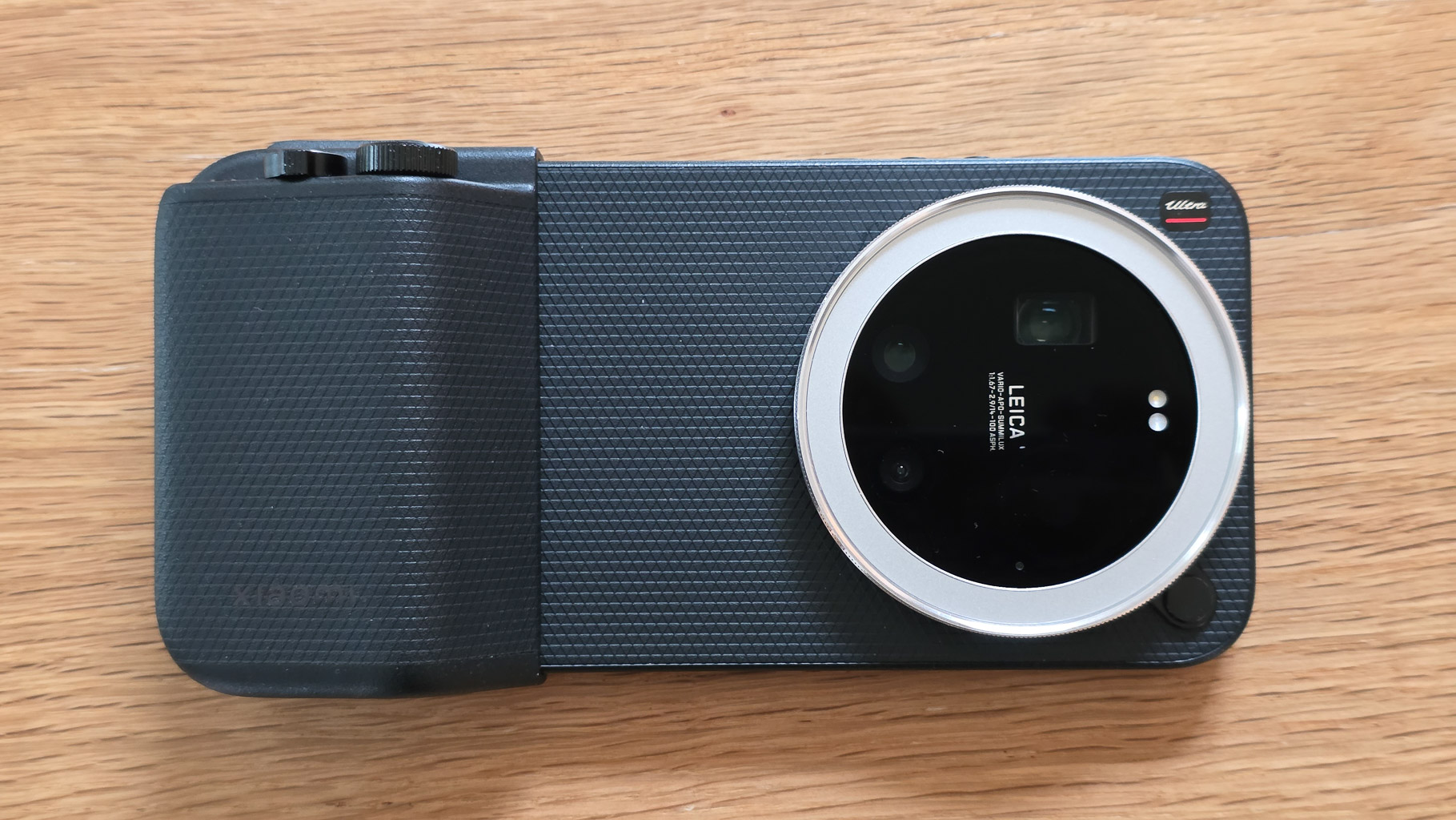 Top view of a black camera featuring a large circular lens and a textured grip, resting on a wooden surface.