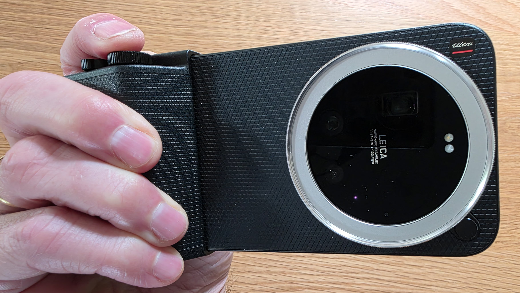 A person holding a Leica camera with a textured grip, showing the lens and control buttons on the top.