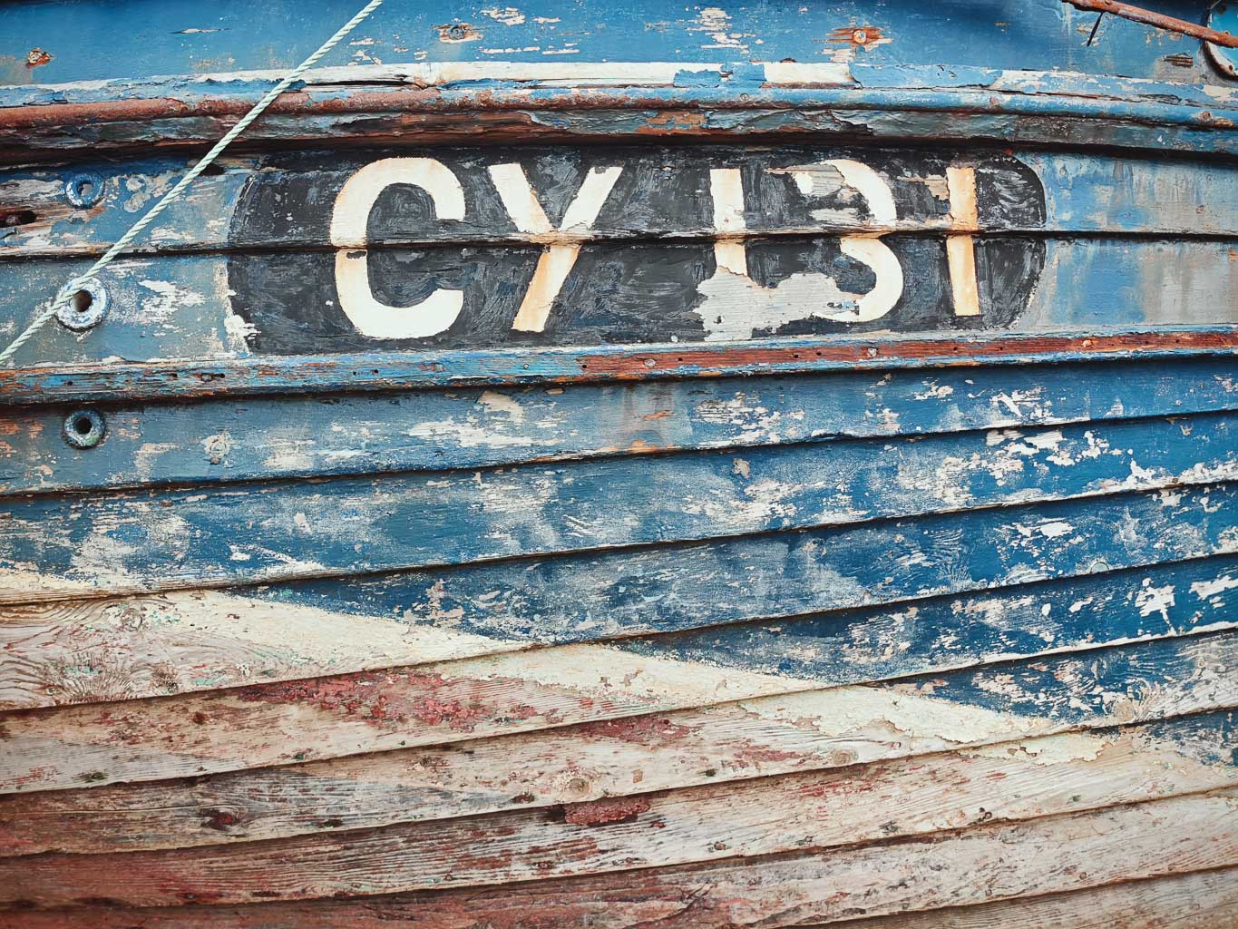 Close-up of a weathered wooden boat with peeling blue paint and the numbers 'CY 131' prominently displayed.
