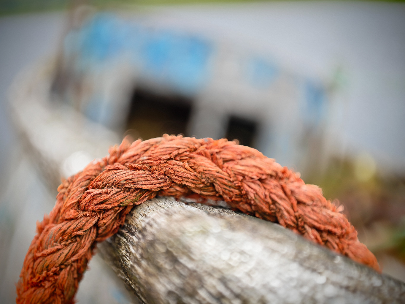 Close-up of a frayed orange rope resting on a weathered wooden surface, with an out-of-focus background suggesting an outdoor setting.