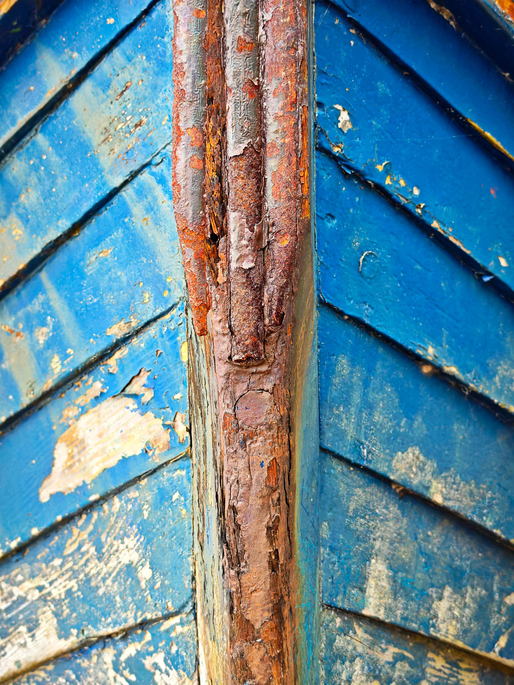Close-up of the bow of a weathered blue wooden boat with peeling paint and rusted metal.