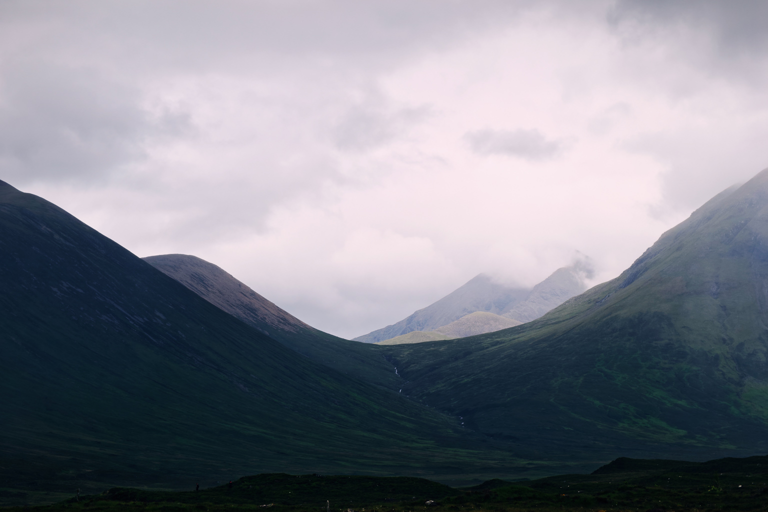 Scenic view of mountains under a cloudy sky, featuring green valleys and peaks partially covered by mist.