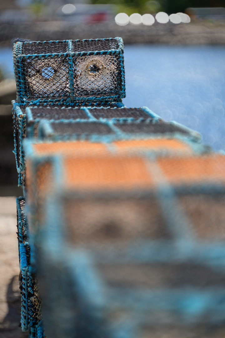 Close-up of stacked crab traps with blue and orange accents, set against a blurred water background.