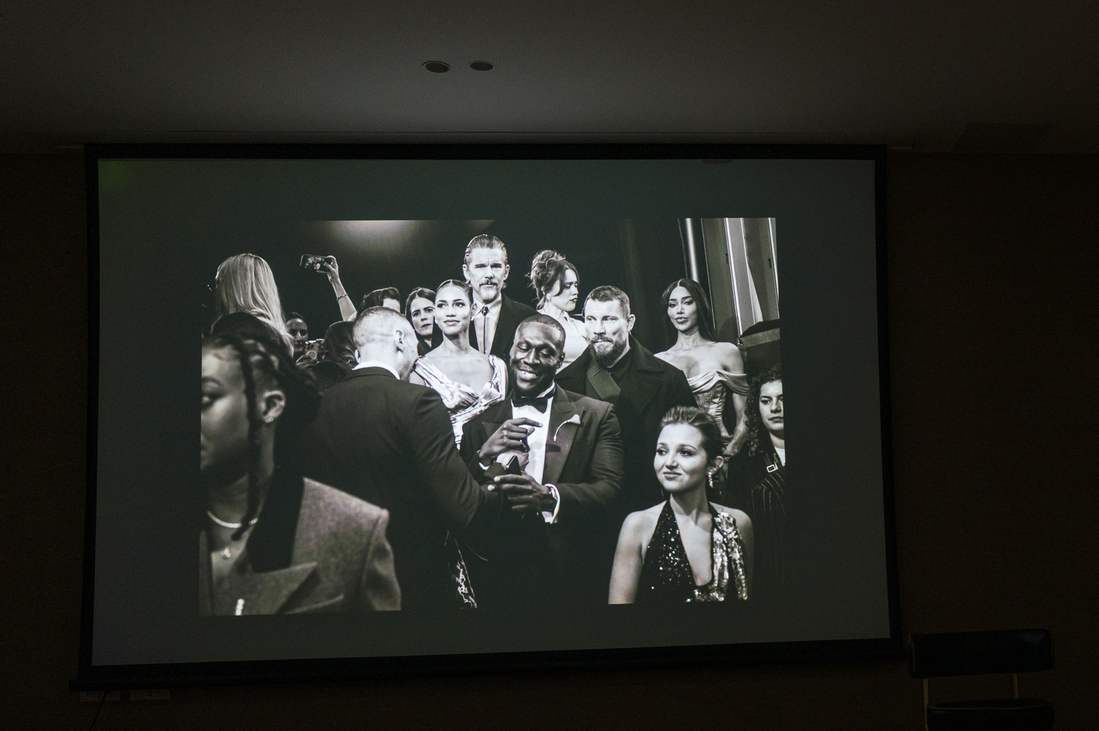 Black and white photograph of a group of elegantly dressed individuals at a social event, with a spotlight effect highlighting their expressions and interactions.
