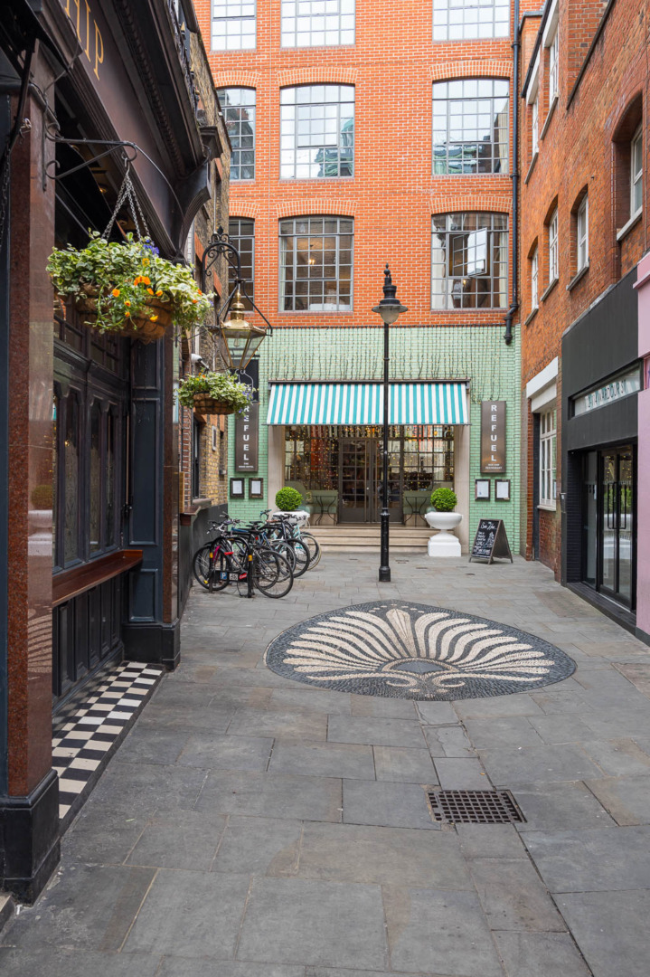 Narrow alley with brick buildings, featuring a cafe with striped awning and a decorative stone pattern on the ground. Bikes are parked along the side.
