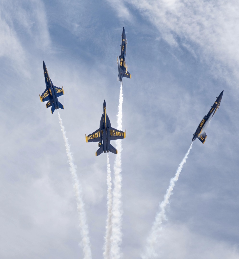 Four blue jet aircraft against a cloudy sky.